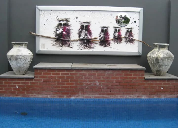 Family Tree: five magpie-owl figures on real branch, long white panel over poolside brick wall. Original painting by Kim Kennedy.